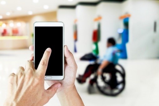 Osoba u invalidskim kolicima i druga osoba drži pametni telefon u rukama.